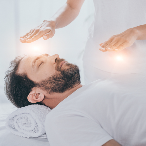 Homme barbu couché avec 2 mains au dessus de lui avec des boules d energie lors d une seance de reiki